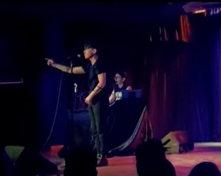 Andrea on stage, again, pointing. My wife Lara is at a keyboard behind them, playing music while they speak. 
