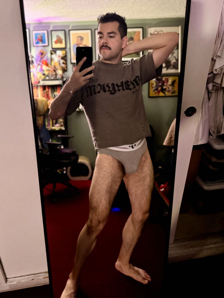 Mirror selfie of man wearing a Mayhem Ball shirt and grey briefs doing a weird flex/pose lifting his arm behind his head and doing some type of lean with his legs