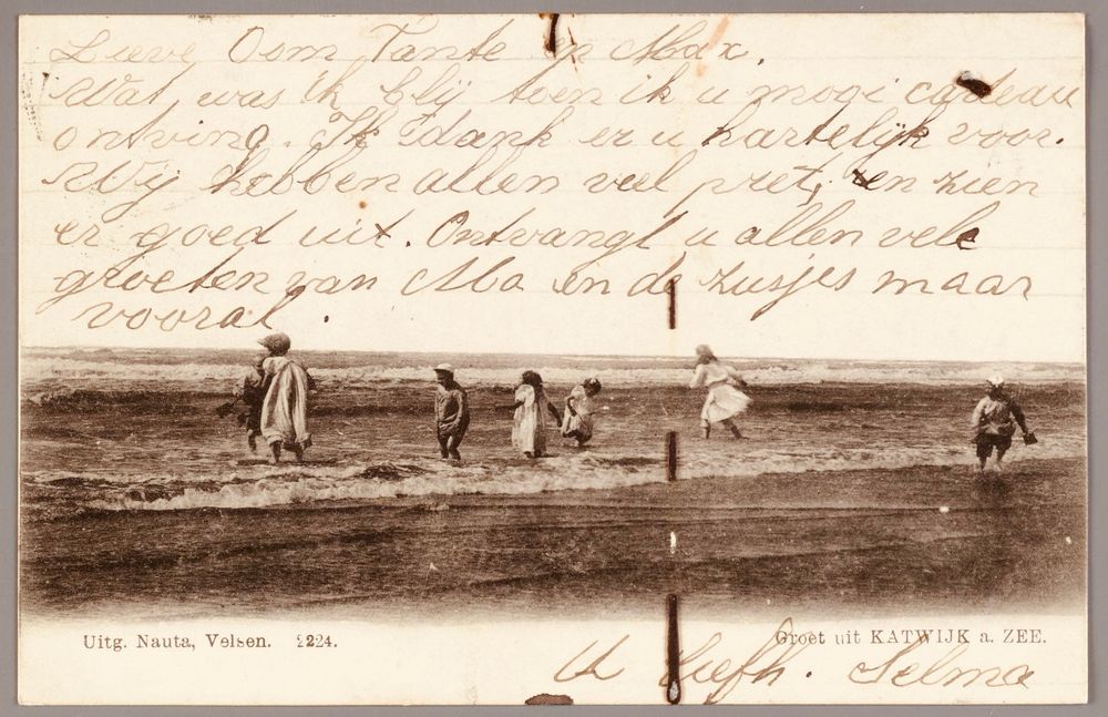 Oude ansichtkaart in zwart-wit met strandgezicht bij Katwijk aan Zee. We zien spelende mensen. Op de kaart staat een handgeschreven tekst van ene Selma aan haar oom en tante waarin bedankt wordt voor een cadeau en het plezier wordt beschreven: “Wij hebben allen veel pret en zien er goed uit.” Bron: Noord Hollands Archief, https://hdl.handle.net/21.12102/FD93B5DEFB8E11DF9E4D523BC2E286E2