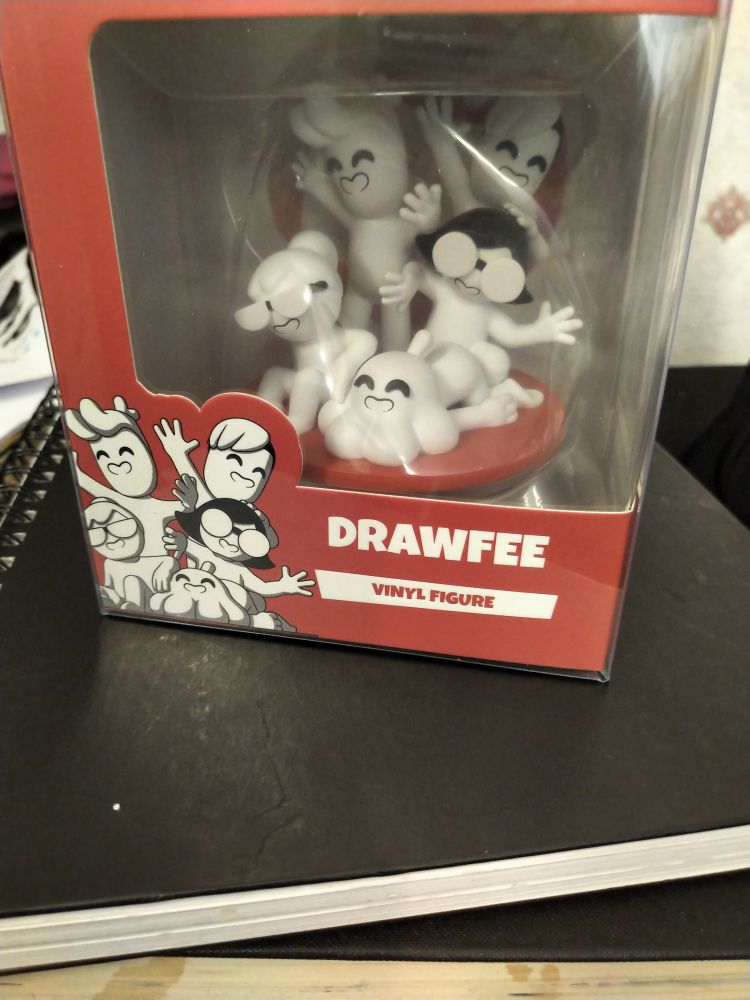 a clear plastic box with red and white packaging on top of some books with the drawfee crew youtooz vinyl figures encased within 