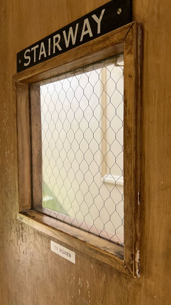 a door with a square window. a sign above the window reads “STAIRWAY”, and there is a small sign (printed on one of those label-maker gadgets) below the window which reads “TO HEAVEN”