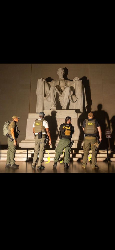 Three men with attire displaying “DEA” on their backs are at the foot of Daniel Chester French’s sculpture of Abraham Lincoln facing it. They appear to be urinating on the steps of the sculpture while to their left another man clad in olive drab military attire stands facing them, observing.