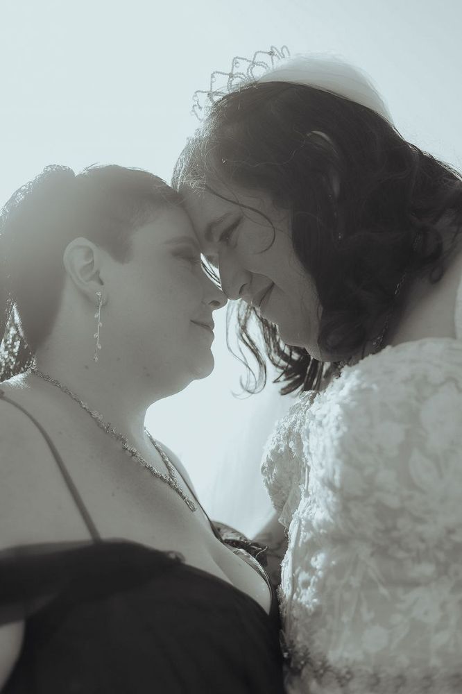 A pair of lesbians on their wedding day, foreheads touching in black and white. It's got some real ethereal vibes