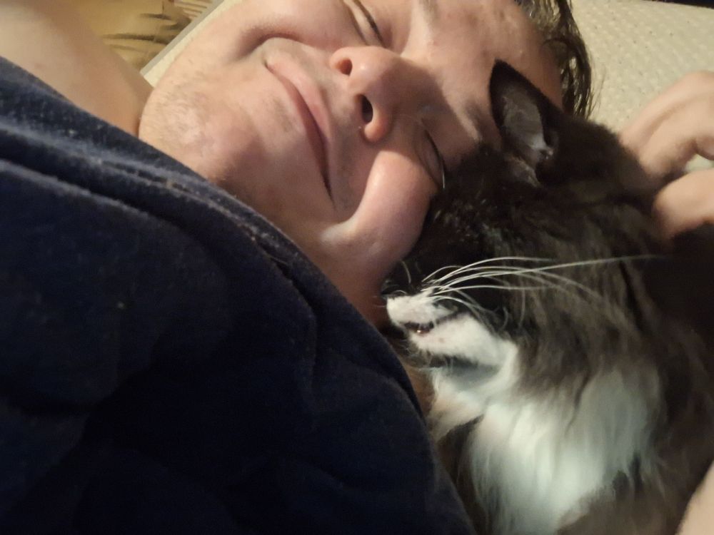 A large homosexual and his long haired back and white cat cuddling together. The cat is pressing his face on the humans cheek.