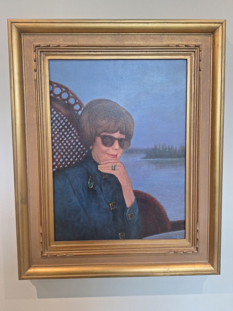 A half-length portrait of an older woman in a blue dress with brown hair, sitting in a wicker peacock chair. She's holding her chin and has on a big blue ring. She's wearing big sunglasses and a smirk.

Nancy Leigh Woodson Spire resided in New York with her husband, Dr. Lyman J. Spire. She generously supported every phase of the museum's growth. Mrs. Spire's posthumous half-length portrait (center) is by Victor DeLor