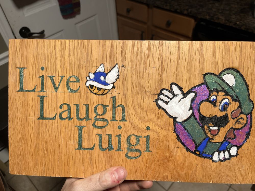A wooden sign hand painted with Live Laugh Luigi along with a blue shell and Luigi from Mario