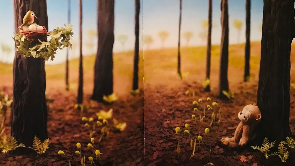 An image from Hank finds an Egg by Rebecca Dudley. Hank, a felt monkey rests by a tree, looking a nest with three eggs and a mother bird tending to it.