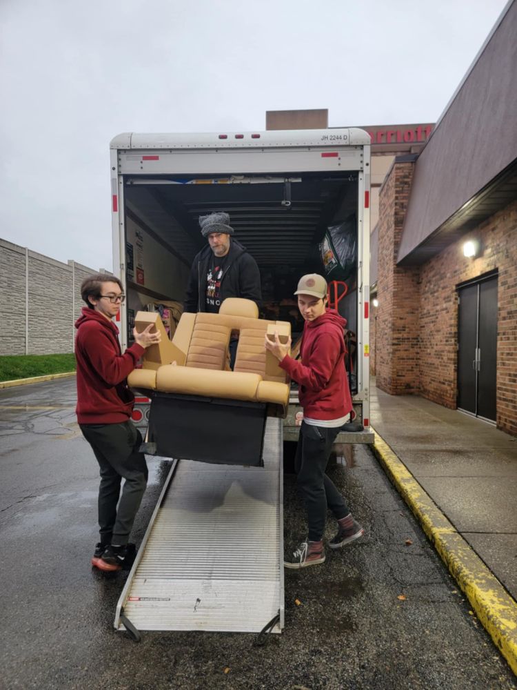 Three guys carrying a captain's chair off a moving truck. 