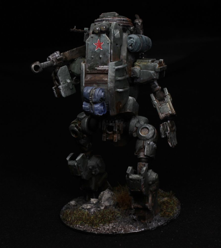 A clunky mech, dusty green with a red star.
It has a large broadsword, and some rolls of fabric attached.
There is a broken statue head on the ground beneath.