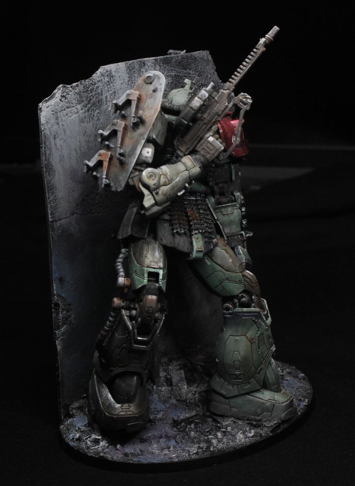 Side view.
There is a large piece of improvised armour (made of a tank's hull part with things that usually hold the wheels), in place of the usual Zaku shoulder shield.
The arm holding the gun is beige, and the lower right leg is brown.