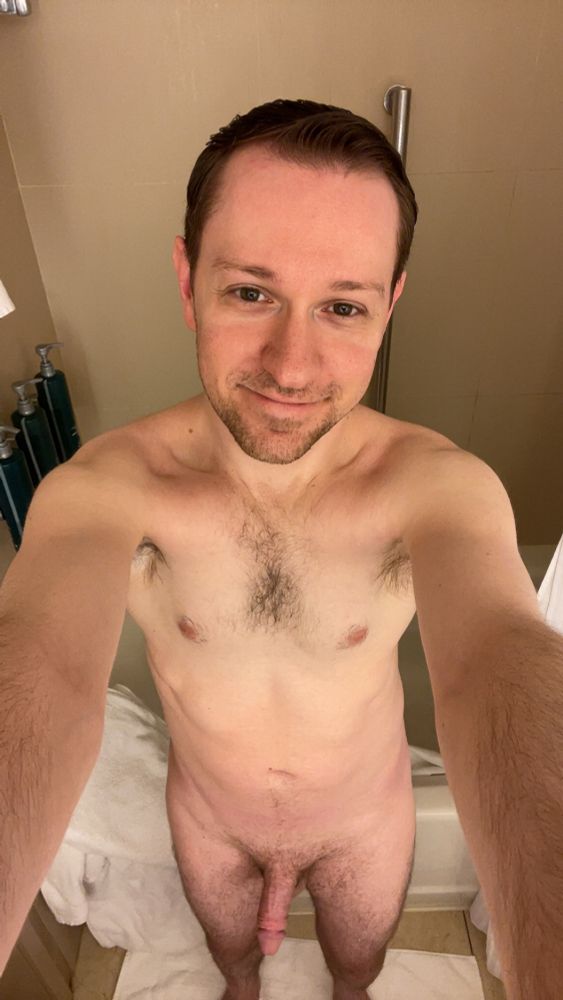 Me standing naked in a bathroom from an overhead angle with white towels on the bath tub ledge behind me