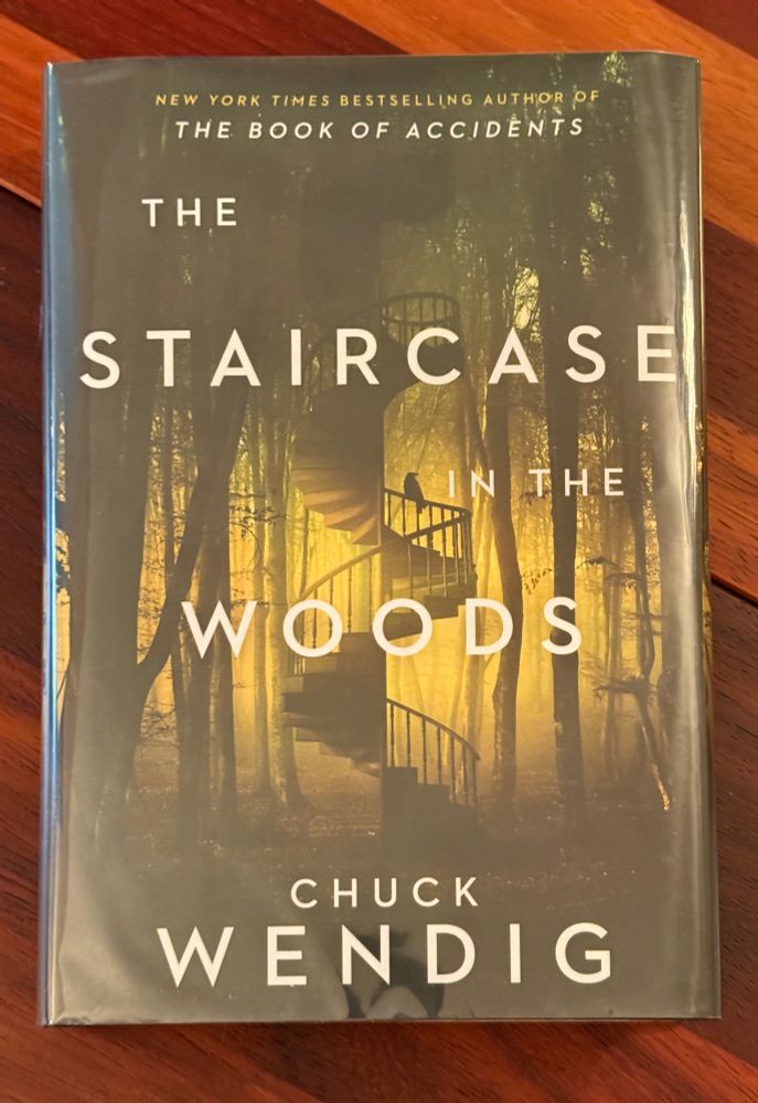 The cover of The Staircase in the Woods by Chuck Wendig. It features a picture of the aforementioned staircase in the woods. There is a bird on the railing about halfway up the spiral staircase. 