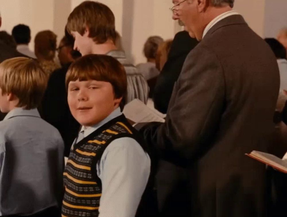 a boy in a striped vest stands in a crowd