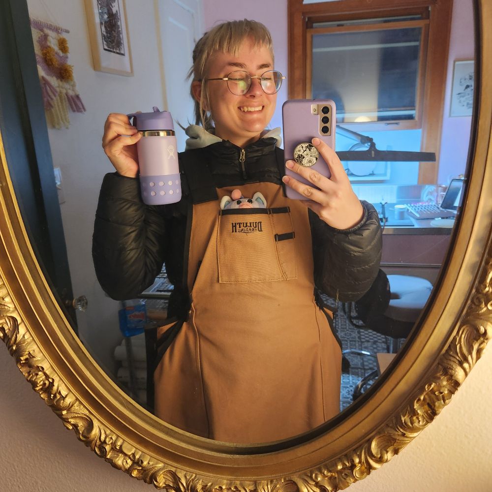 Picture of me holding up a kid sized hydro flask in light purple color scheme, smiling over how small and cute it is
