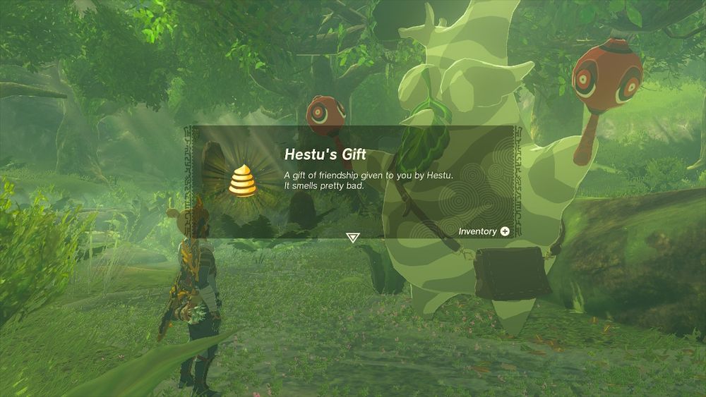 A screenshot from The Legend of Zelda: Tears of the Kingdom. The background shows Link and Hestu in Korok Forest, with a pop-up in the foreground showing a golden poo with the accompanying text "Hestu's Gift: A gift of friendship given to you by Hestu. It smells pretty bad."