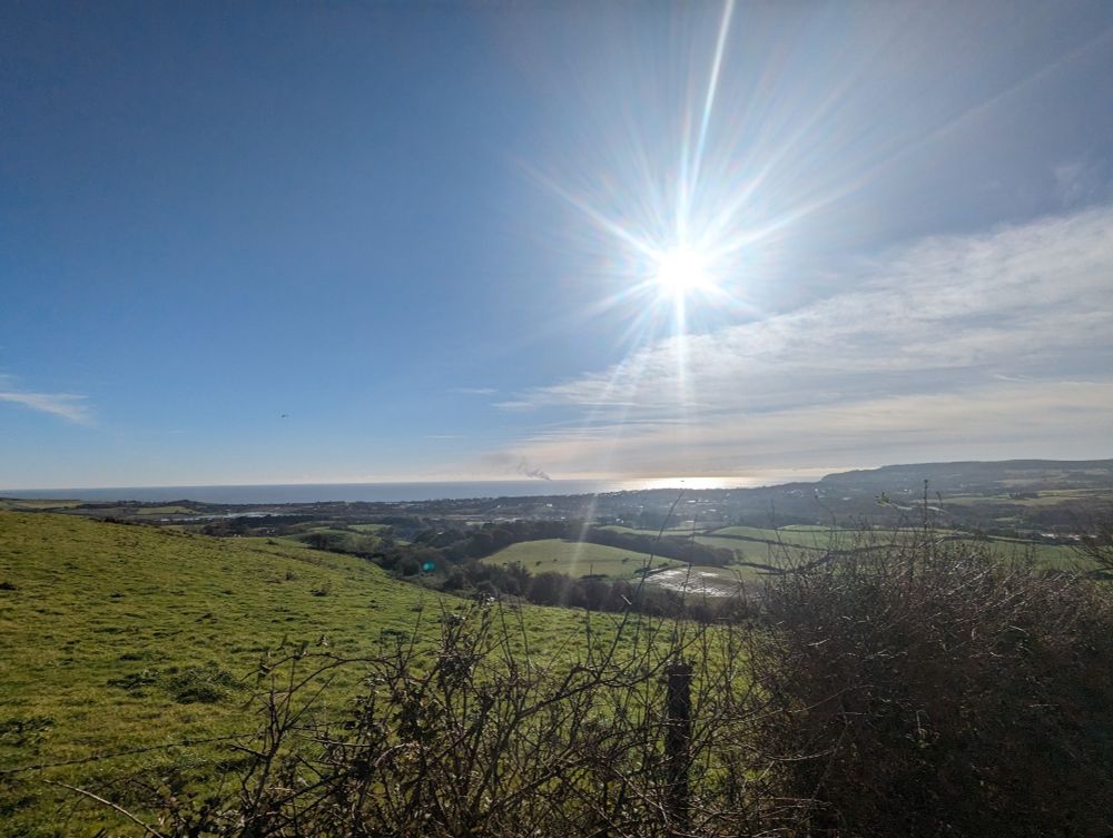 Rolling green hills of the isle of Wight with some lens flare. In the distance on the solent you can see a few whisps of smoke