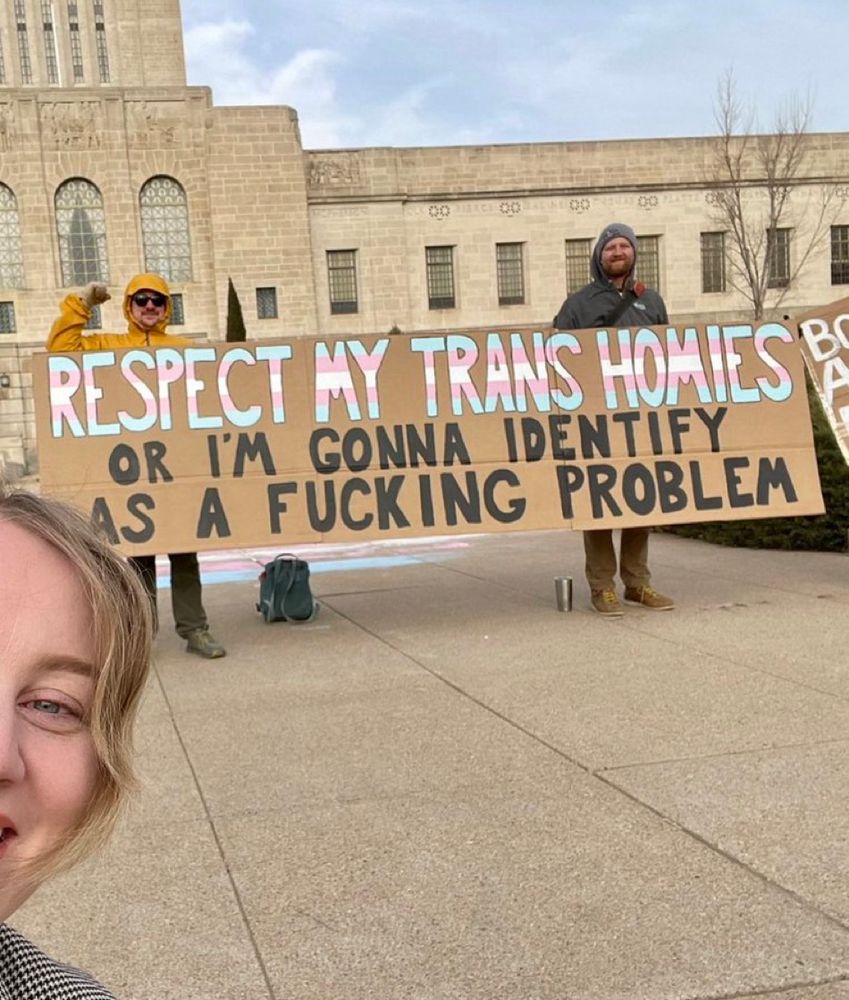 Nebraska state Senator Megan Hunt standing in front of a sign reading “RESPECT MY TRANS HOMIES OR I'M GONNA IDENTIFY
AS A FUCKING PROBLEM”