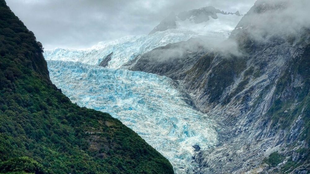 Melting glacier with mist and green hill in the foreground