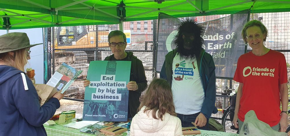 A Sheffield Friends of the Earth stall with 3 people behind the stall and an adult and child in the front