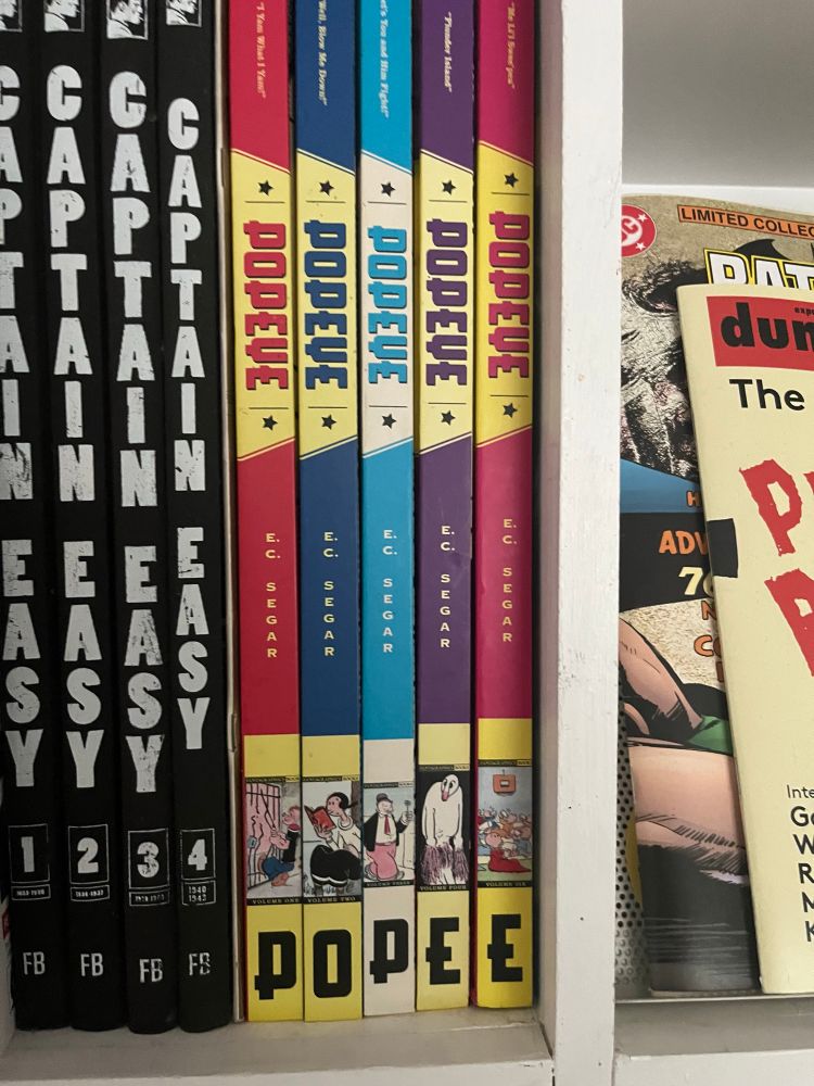 Bookshelf with copies of the Fantagraphics captain easy & Popeye books. The first issue of DUMMY magazine and a Batman treasury poke into view from the right  