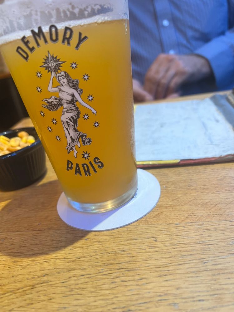 A glass containing a pale, cloudy beer, with Demory Paris decal. 