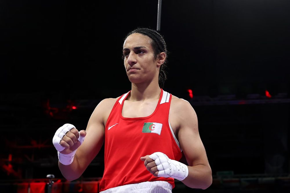 Armenian boxer Imani Khelif, in a red tank top with wrapped hands. She has very small breasts on a not-so-small chest. 