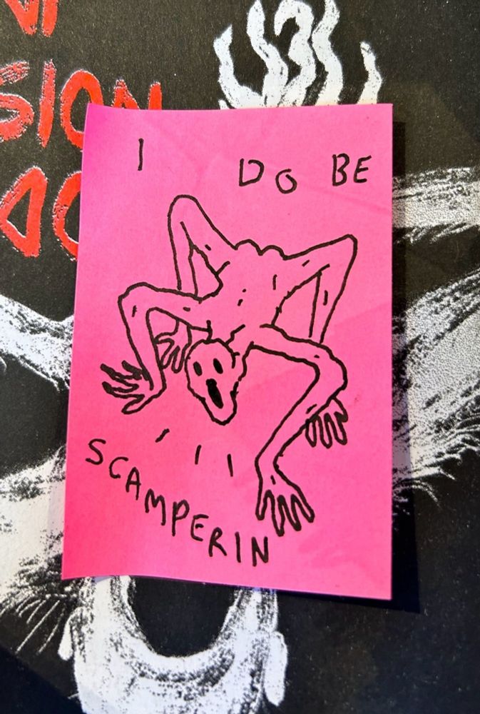 a pink post-it note i drew on, there's a crude little weird guy on all fours, it looks like he's hollering. it says I DO BE SCAMPERIN