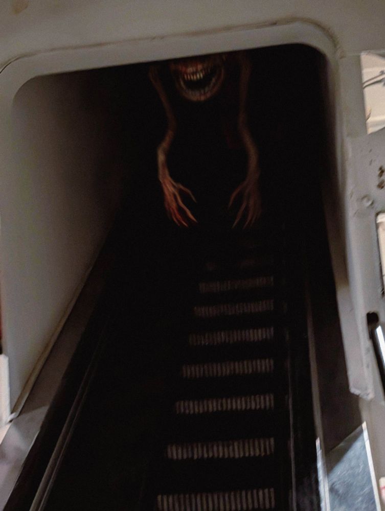 an escalator ascending into darkness. a hanging creature, only its wide mouth of flat teeth is visible, hangs long gangly arms down to grab you