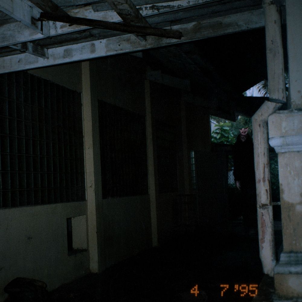 a photo of a dark outdoor alleyway. in the back stands a man with his head bisected at the eye sockets.