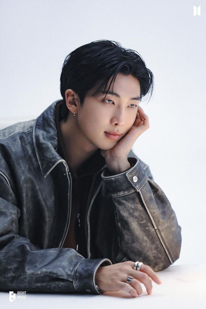 Kin Namjoon sitting, leaning on his hand on a white background.