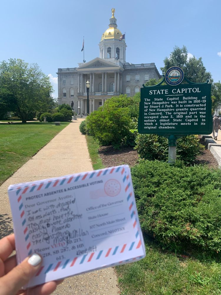 Olivia of OpenDemocracy holding postcards asking Governor Ayotte to veto SB 287 in front of the NH State House
