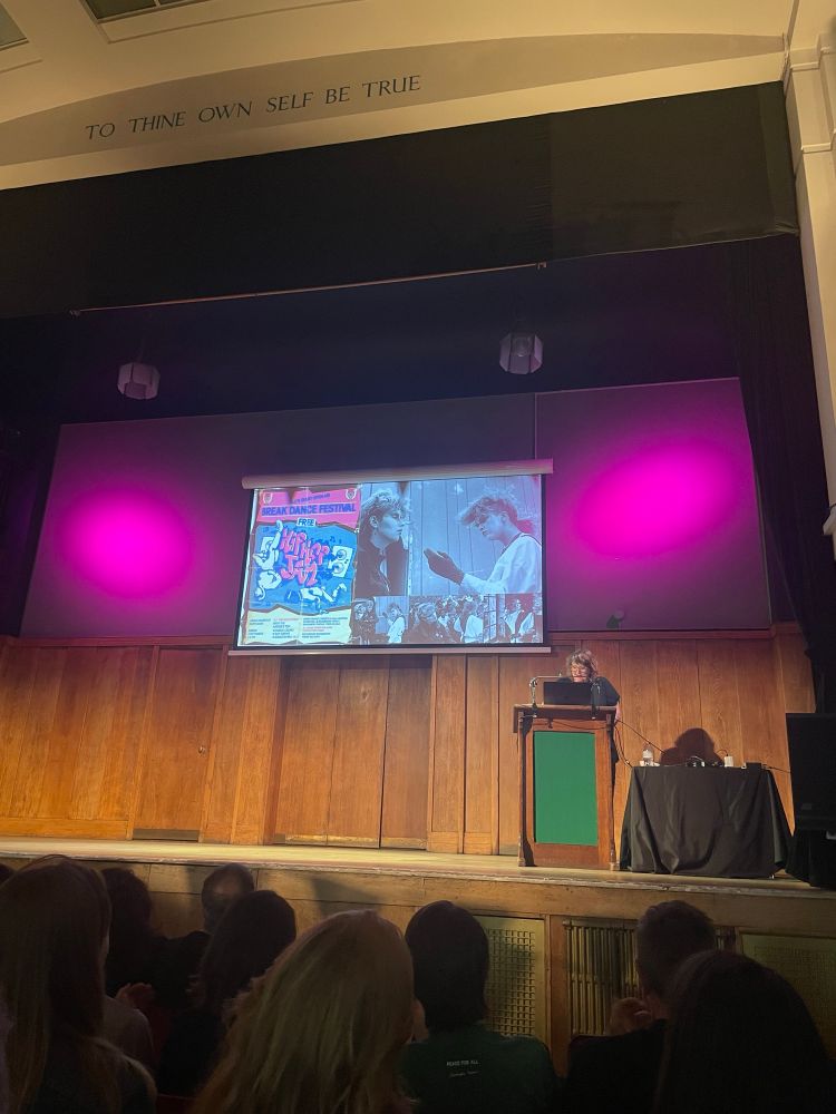 A different woman is speaking stage her slide is FILLED with photos of her dressed as a robot in the 80s and posters of gigs  because she was a Teenage Robot Dancer 
