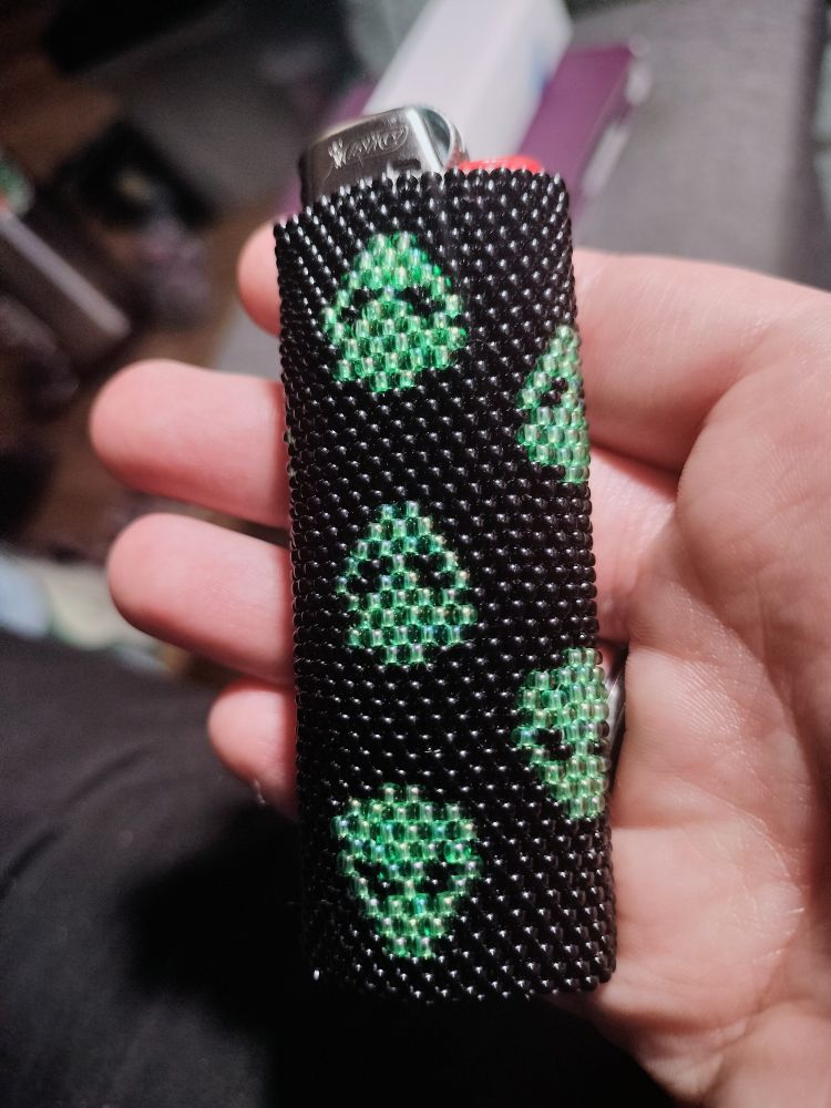 Lighter case made of 11/0 miyuki beads. There's a black background with little green alien heads facing different directions