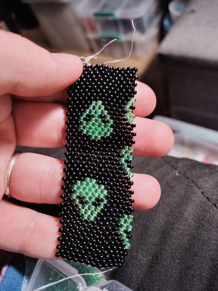 Even count peyote stitch - green alien faces on a black background made with size 11/0 miyuki/Czech beads. A bit wonky but I'm basically freehanding it and I just wanted to make alien faces, ok? 😵 it's going to be a lighter cover.