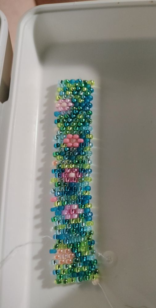 Rows of peyote stitched beads, blue/green background with little pink flowers