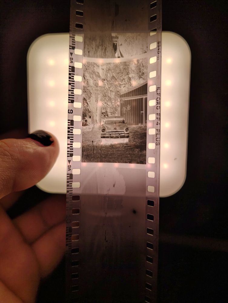 A black and white 35mm negative of a 50s car shot in portrait orientation held over a small led lamp
