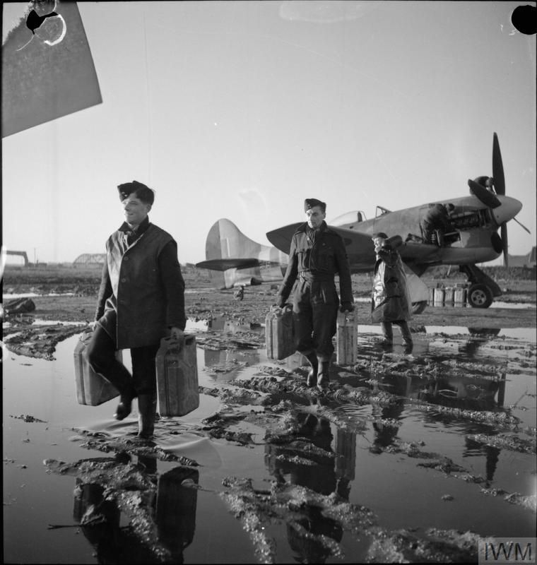 Ground crew servicing and refuelling a Hawker Tempest Mark V of No. 56 Squadron RAF in flooded conditions after the heavy rains at B80/Volkel, Holland. 📷 IWM CL 1676 (Amid deep mud and large puddles, two men carry jerrycans away from a parked Tempest. Another man carries an oxygen bottle, while two more are working on the engine)