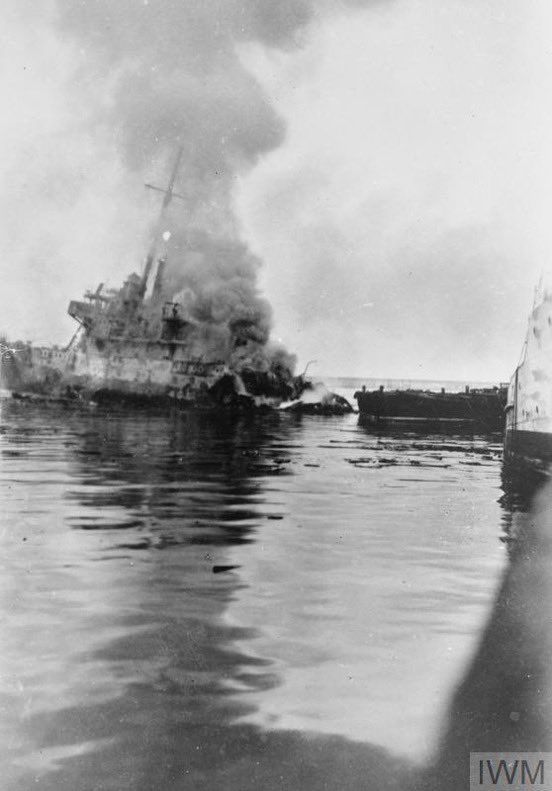 HMS Hartford on fire and sinking at the conclusion of Operation RESERVIST. This photograph shows a small warship, with her stern destroyed by an explosion, burning fiercely and listing to starboard.