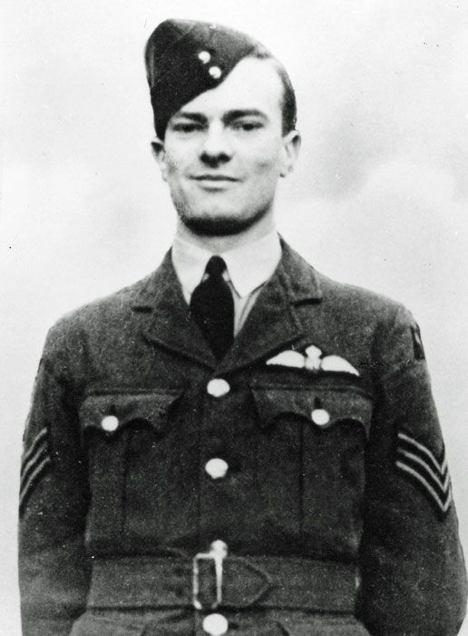 Smiling RAF sergeant pilot, standing with his hands at his sides for a portrait photograph.