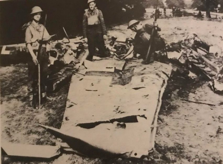 Three soldiers picking through the wreckage of a crashed aircraft. The underside of a wing bearing the German cross is in the foreground.