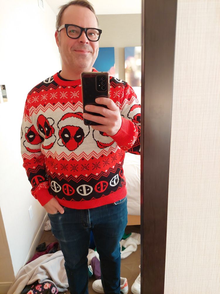 Man wearing ugly Christmas sweater featuring comic book character Deadpool.