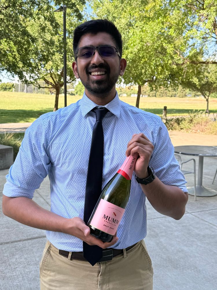 A PhD student successfully defended his qualifying exam at UC Davis and is holding a bottle of champagne. 