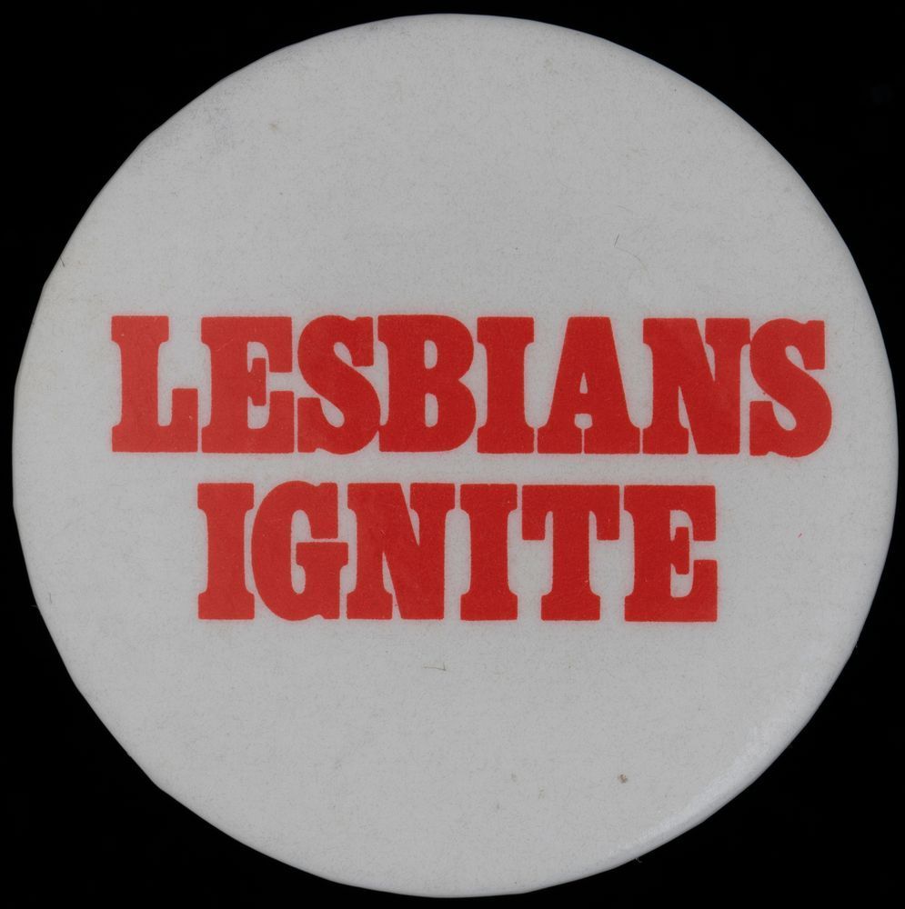 White badge pin with bold red text reading “LESBIANS UNITE.”