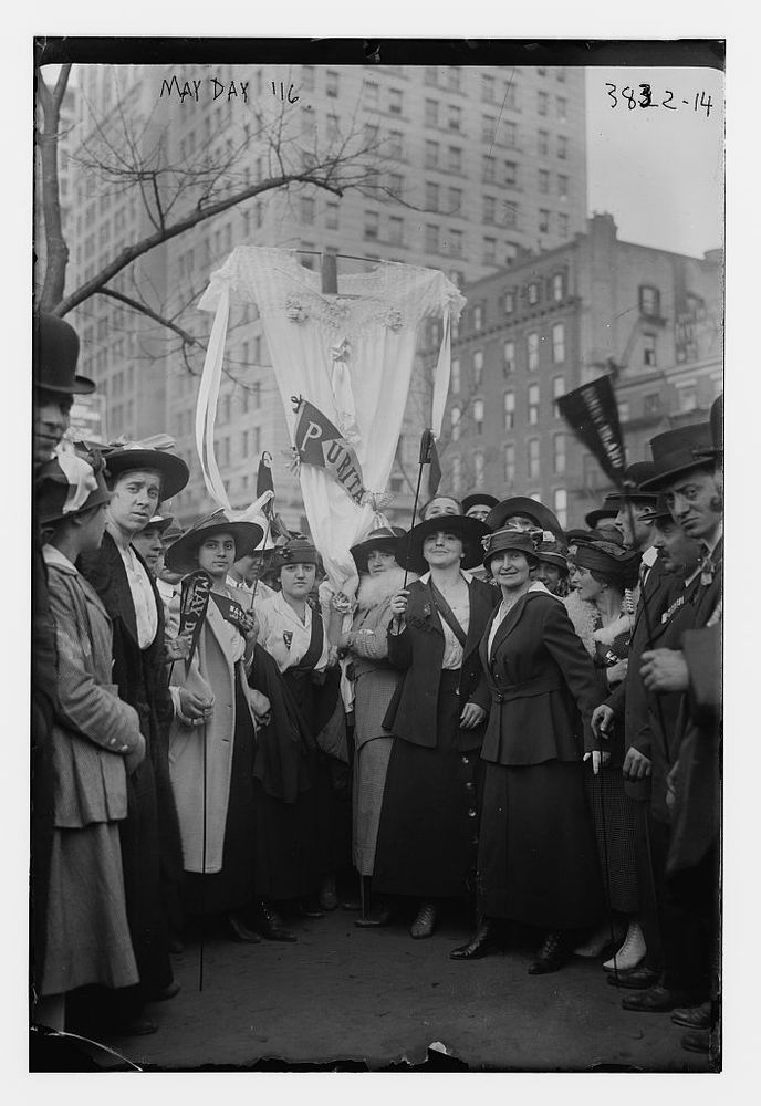 Black and white photograph of people in Chicago dressed in suits and long dressed holding banners which say May Day and a few other things which aren't legible