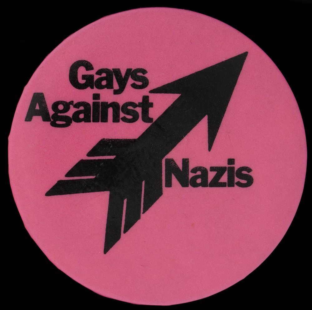 Pink badge pin with a bold graphic arrow pointing up at a diagonal with text reading "Gays Against Nazis"