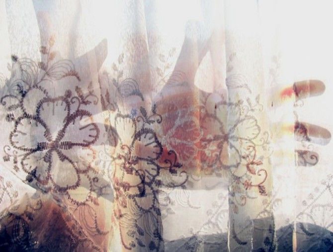 an over exposed photo of a translucent curtain with flowers embroideries and a hand shining through from the other side of the curtain.