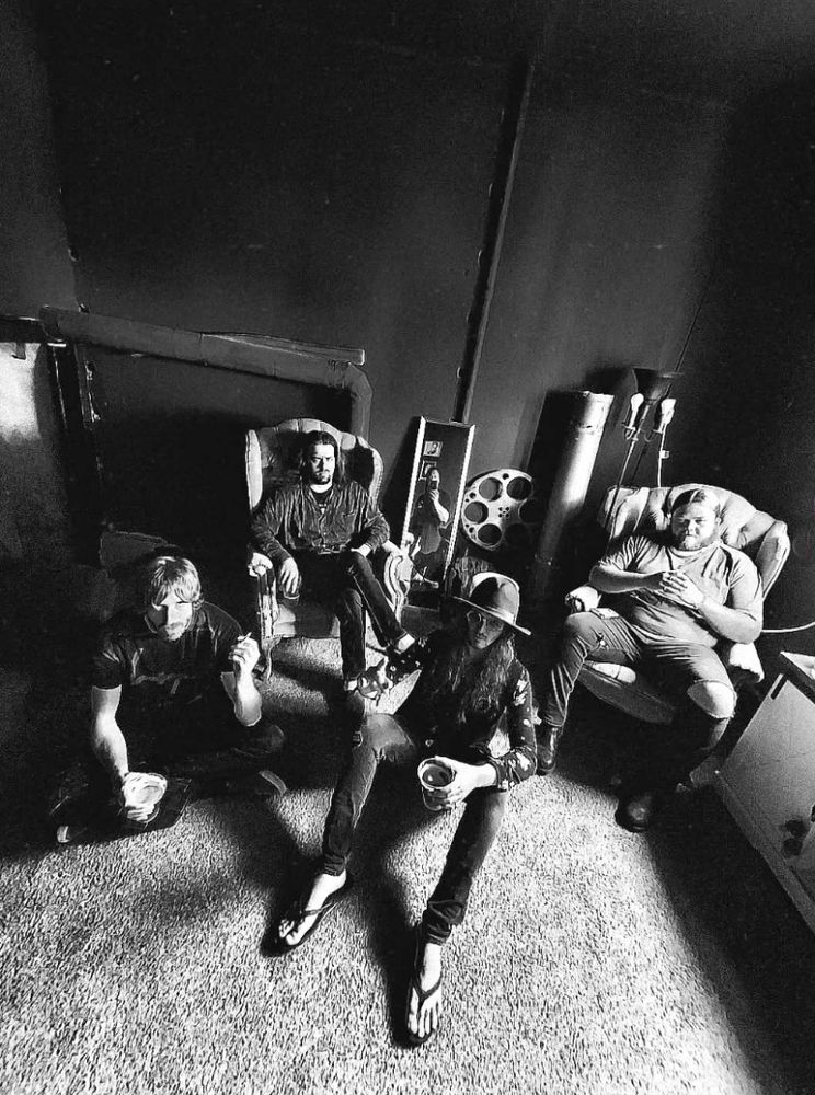 Black and white photo of The Velvet Snakes shot from above as the four musicians sit on the floor and in chairs.