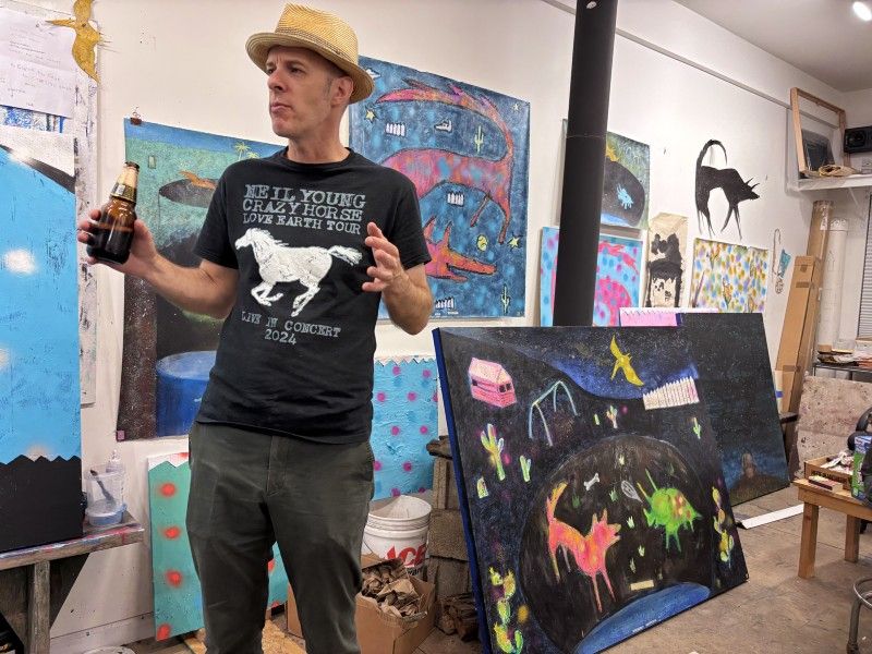 Dylan Strzynski in his studio, with numerous paintings behind him.