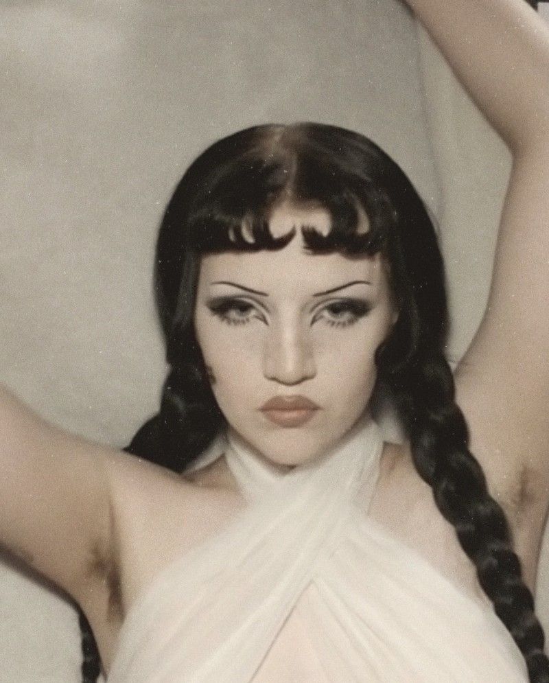 Dollie Rot holds her arms above her head and wears a white dress.