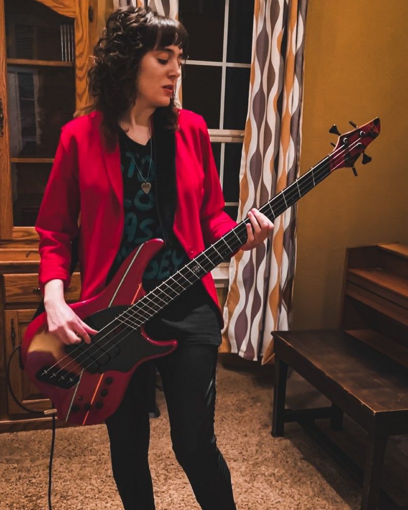 Kelsey Detering wears a red jacket and plays a red bass guitar.